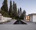 Preview of Northwest Reflections - Image 7: concrete wall, concrete floor, modern architecture, pool, minimalistic design, flat roof, outdoor space, landscape design, patio, pathway, greenery, exterior lighting, large windows, open space, wood accents, reflection, poolside, symmetry, sleek design, contemporary home.