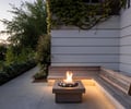 Preview of Northwest Reflections - Image 9: fire pit, concrete floor, outdoor seating, wood bench, lighting, garden path, patio, wall cladding, ivy, modern architecture, landscaping, stone accents, evening setting, cozy atmosphere.