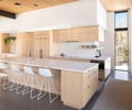 Preview of Sun Valley Fireweed - Image 27: kitchen, concrete floor, island, marble countertop, wooden cabinets, open shelves, modern design, pendant lighting, large windows, bar stools, stainless steel faucet, integrated appliances, minimalist, natural light, warm tones, ceiling beams.