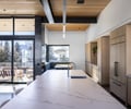 Preview of Sun Valley Fireweed - Image 28: kitchen, marble countertop, wood cabinets, large windows, sliding glass doors, patio, outdoor seating, pendant lighting, open floor plan, natural light, modern design, stainless steel faucet, wooden ceiling, mountain view, minimalist, dining nook, integrated appliances, deck, railing, indoor-outdoor connection.