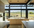Preview of Sun Valley Fireweed - Image 30: kitchen, large windows, natural light, wooden cabinets, modern design, panoramic view, landscape, countertops, interior design, open space, minimalistic, sleek handles, integrated appliances, mountain view, outdoor-indoor connection, clean lines, bright interior, glass panels, neutral tones.