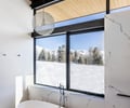 Preview of Sun Valley Fireweed - Image 33: bathroom, bathtub, freestanding tub, marble wall, large window, black window frame, wood ceiling, pendant light, modern design, outdoor view, natural light, minimalist, stone texture, contemporary style, luxury bathroom, sleek faucet, snow landscape.