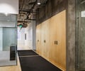 Preview of Undead Labs - Image 3: interior design, commercial space, concrete wall, wood panels, carpet flooring, recessed lighting, ceiling pipes, glass door, modern, hallway, corridor, visible ductwork, steel frame door, minimalist, texture contrast, ambient lighting.