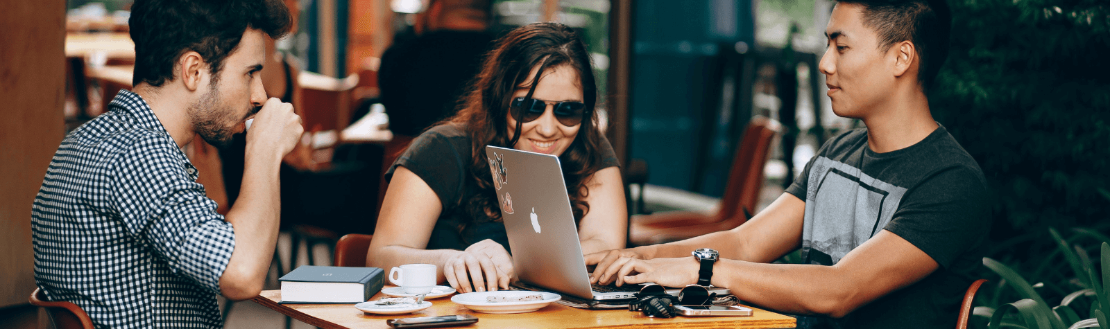 Two men and a woman at a table in coffee shop looking at a one man's laptop - Employee Digital Experience.