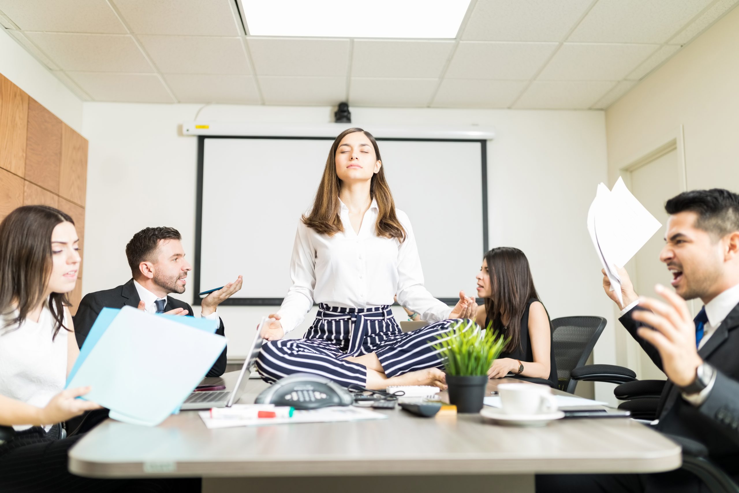 Young businesswoman meditating in lotus position while colleagues yelling during negotiation in office.