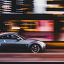 A silver sports car speeding through a city at night, the buildings and lights behind it blurred into streaks of orange and pink.