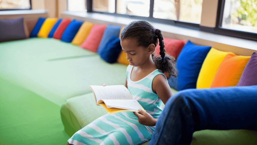 menina lendo um livro em espaco infantil colorido