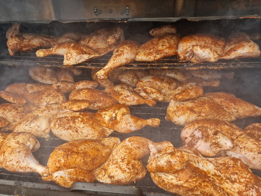 Chicken pieces seasoned and cooking on a large BBQ grill, with smoke rising from the hot coals below