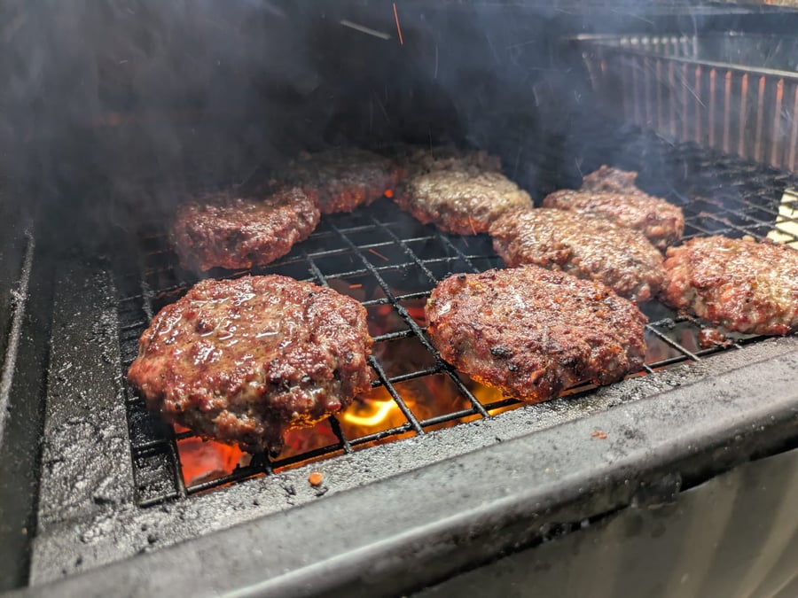 Juicy beef burgers sizzling on the grill over hot coals, with smoke rising, perfect for any event
