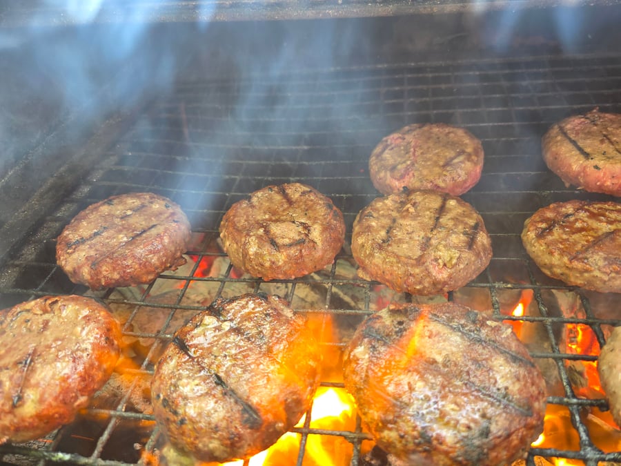 Juicy burgers sizzle on the grill over hot coals, with smoke rising, ready for a delicious BBQ feast