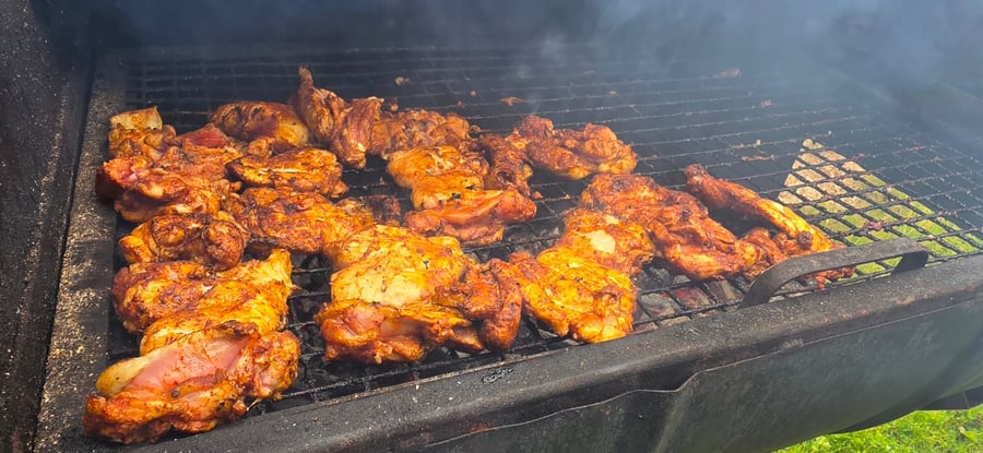 Marinated chicken pieces sizzling on a large BBQ grill, with smoke rising, ready for a delicious outdoor event
