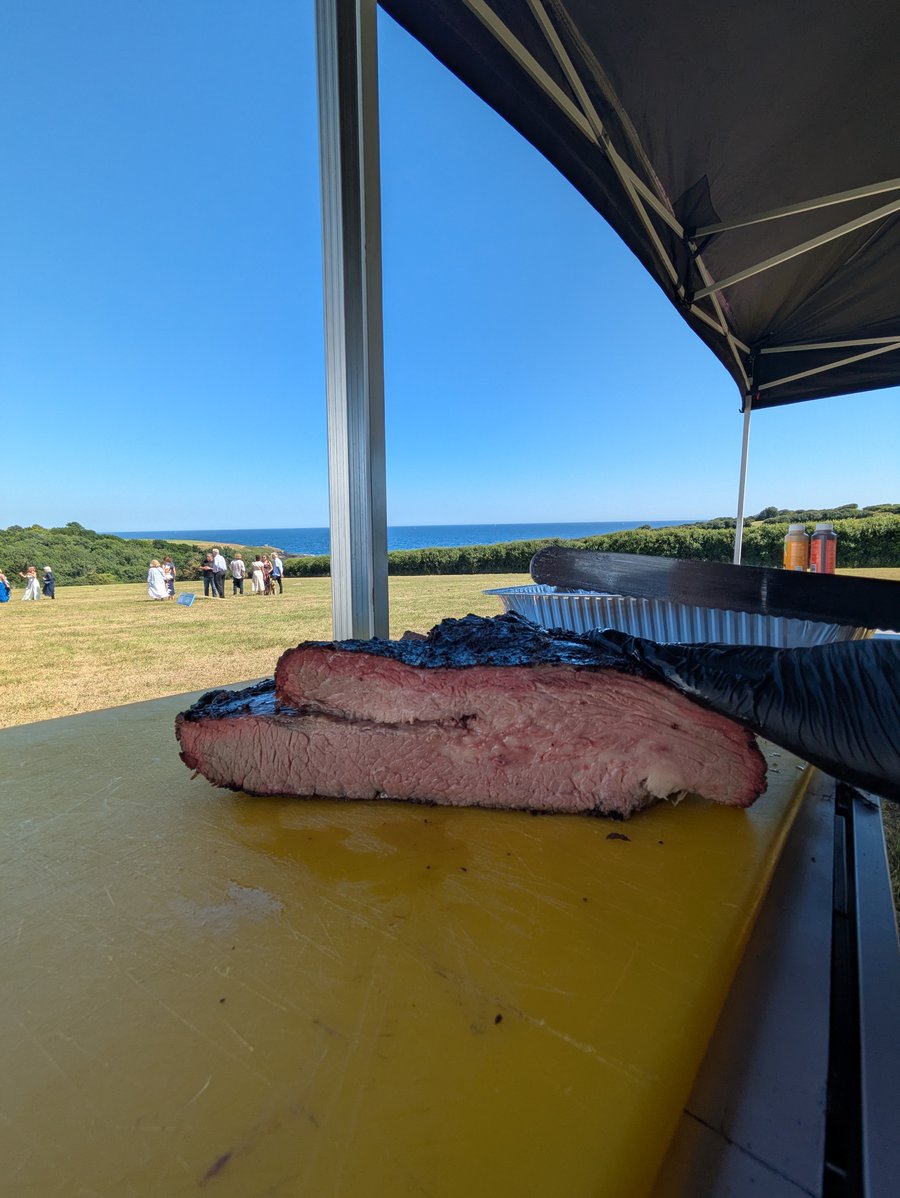 A perfectly smoked brisket, sliced and ready to serve at a beautiful outdoor event overlooking the sea