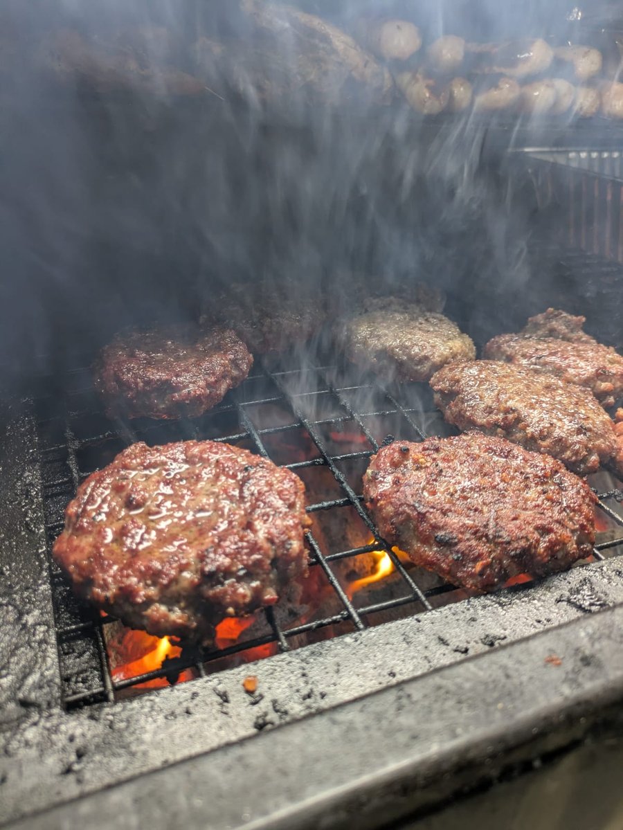 Juicy burgers and other meats sizzling on the grill over hot coals, with smoke rising, ready for a delicious BBQ feast