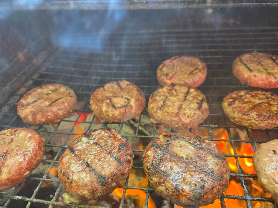 Succulent burgers sizzling on the grill over hot coals, ready to be served at your next event