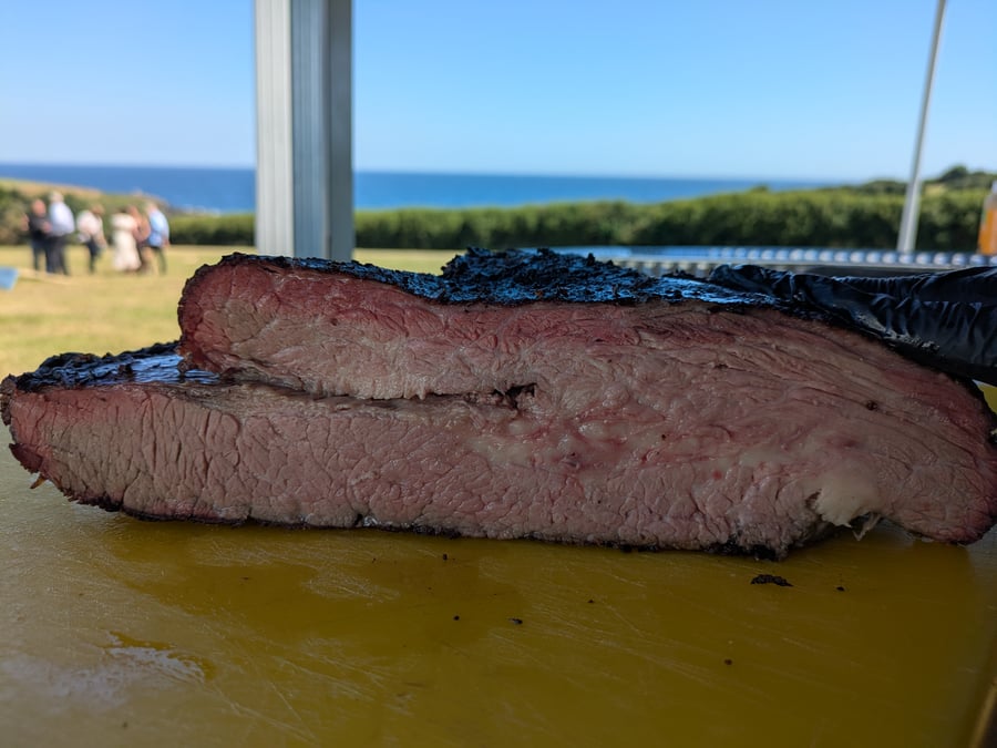 Perfectly smoked brisket, showing a beautiful smoke ring, ready to be served at a coastal event