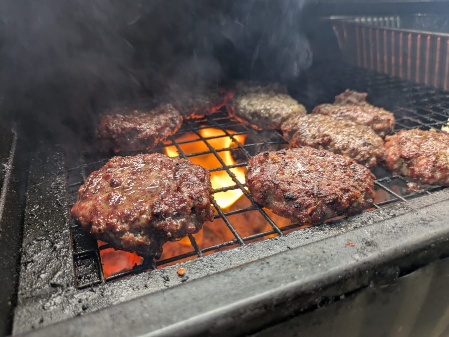 Juicy beef burgers sizzle over hot coals on a BBQ grill, with smoke rising as they cook to perfection