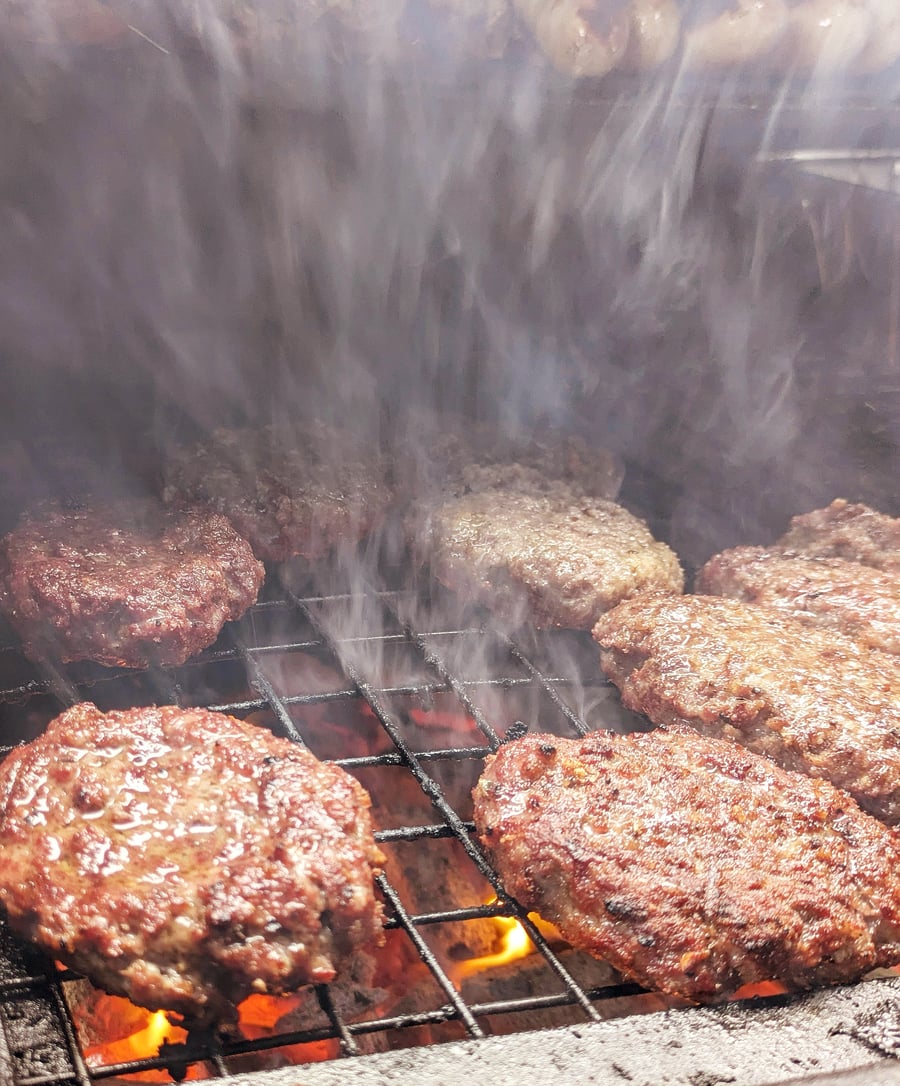 Juicy burgers sizzling on the grill with smoke rising, perfect for a live-fire event