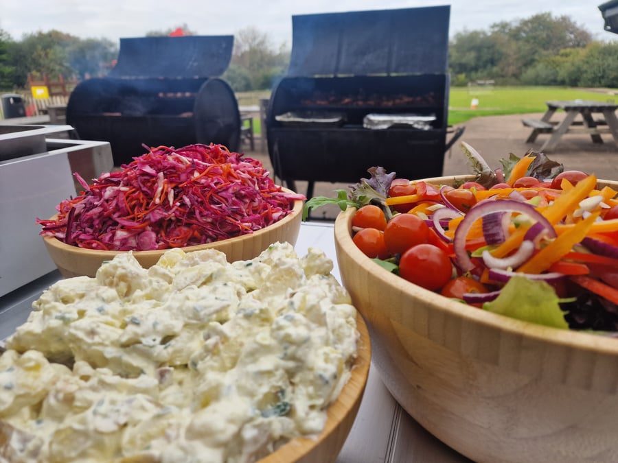 Freshly prepared salads and potato salad accompany a delicious BBQ spread cooked on site for an outdoor event