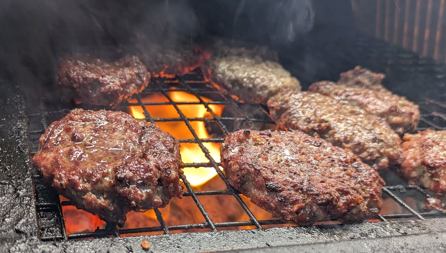 Juicy beef burgers sizzling on the grill over hot flames, perfect for a live-fire BBQ event