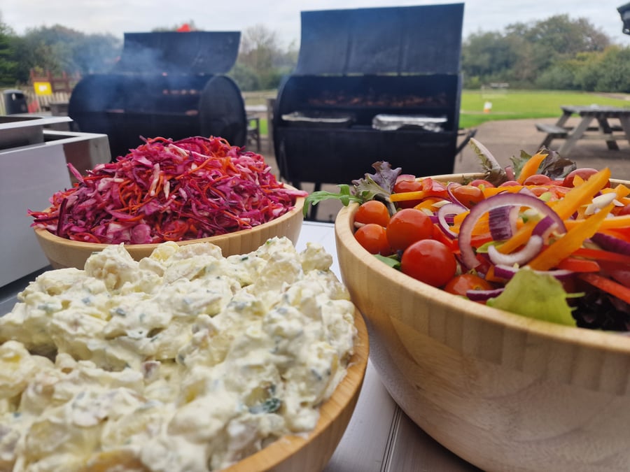 Freshly prepared salads and coleslaw accompany a delicious BBQ spread cooked on site for an outdoor event
