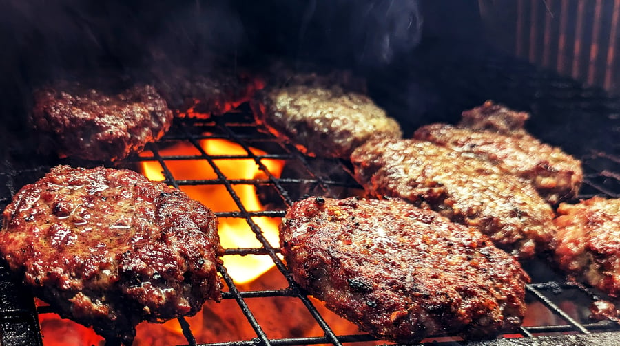 Juicy burgers sizzle over hot coals on the grill, ready for a delicious live-fire BBQ event