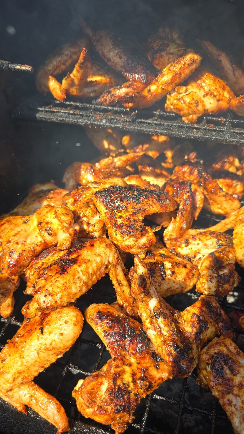 Deliciously seasoned chicken wings and drumsticks cooking on a smoky BBQ grill, perfect for any outdoor event