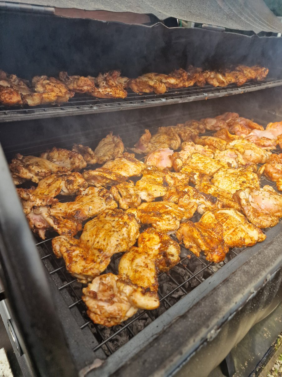 Marinated chicken pieces cooking on a large BBQ grill, with smoke rising from the coals below