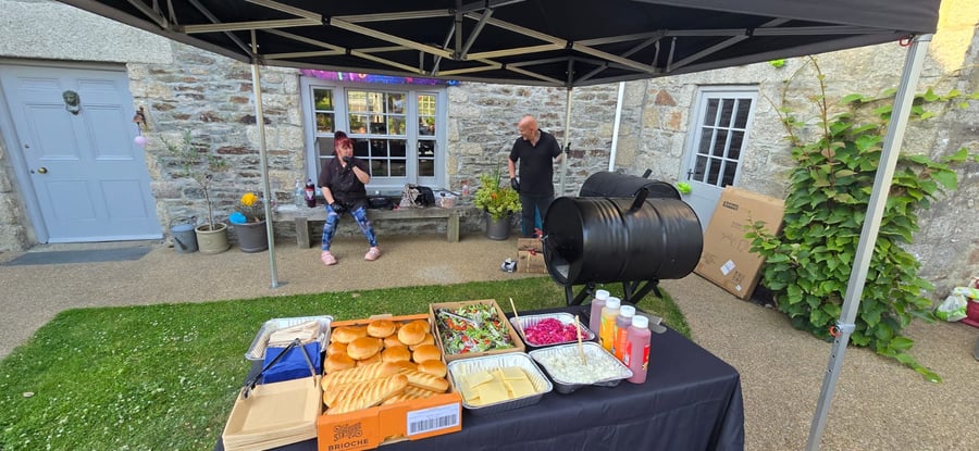 A BBQ setup with a variety of buns, salads, cheese, and sauces, ready for serving at an outdoor event