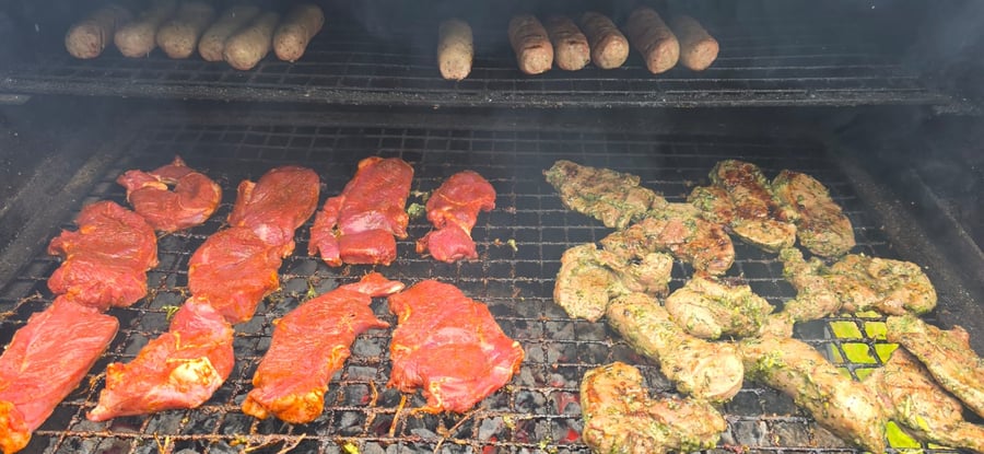 Marinated meats and sausages sizzling on the grill, ready for a delicious live-fire BBQ event