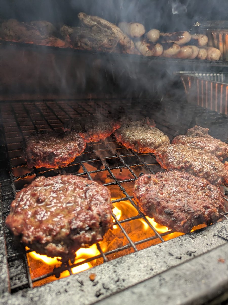 Succulent burgers and sausages sizzling over hot coals on a BBQ grill, with smoke rising from the delicious food