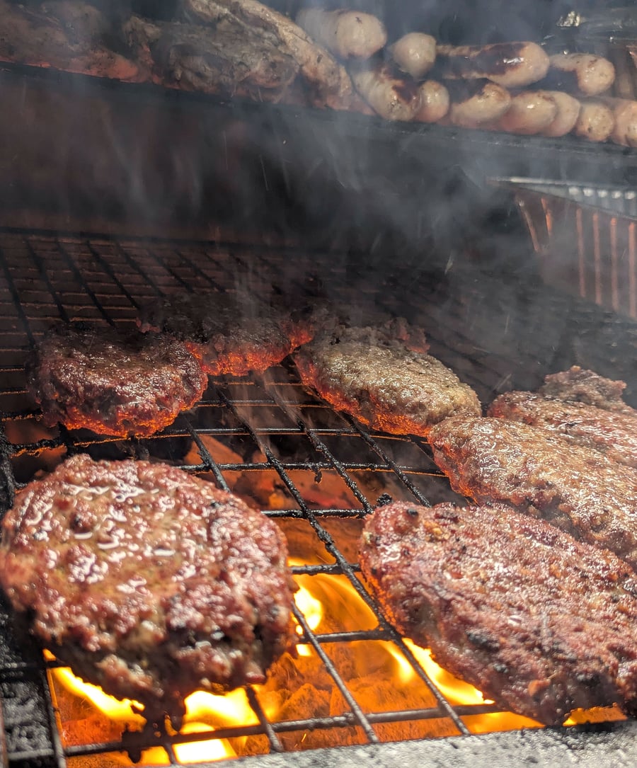 Succulent burgers and sausages sizzling over hot coals on a BBQ grill, with smoke rising from the delicious food (2)