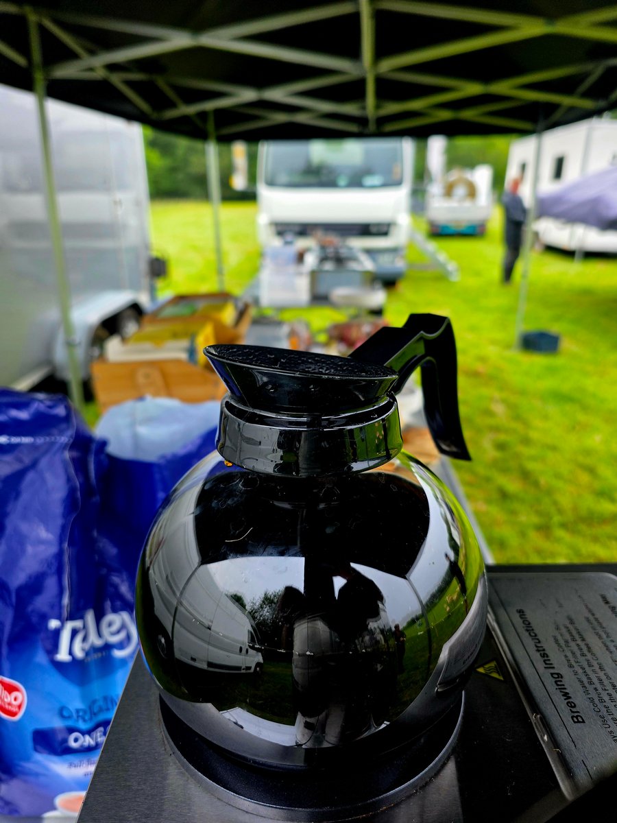 A coffee pot and catering supplies at a film or TV production unit base, with vehicles and a gazebo in the background