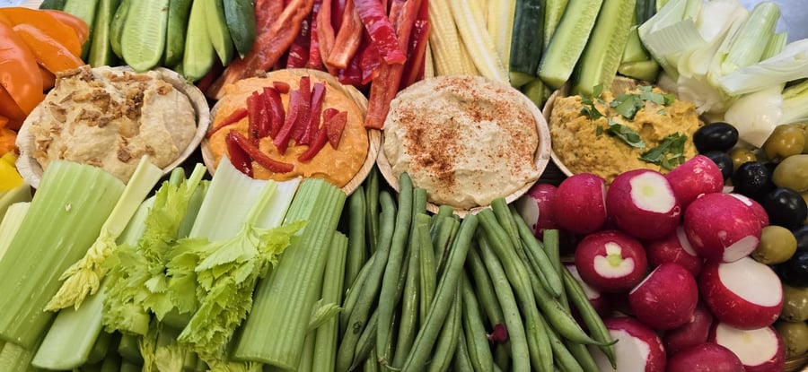 A vibrant buffet spread featuring fresh crudités, including celery, cucumber, peppers, radishes, and green beans, served with a selection