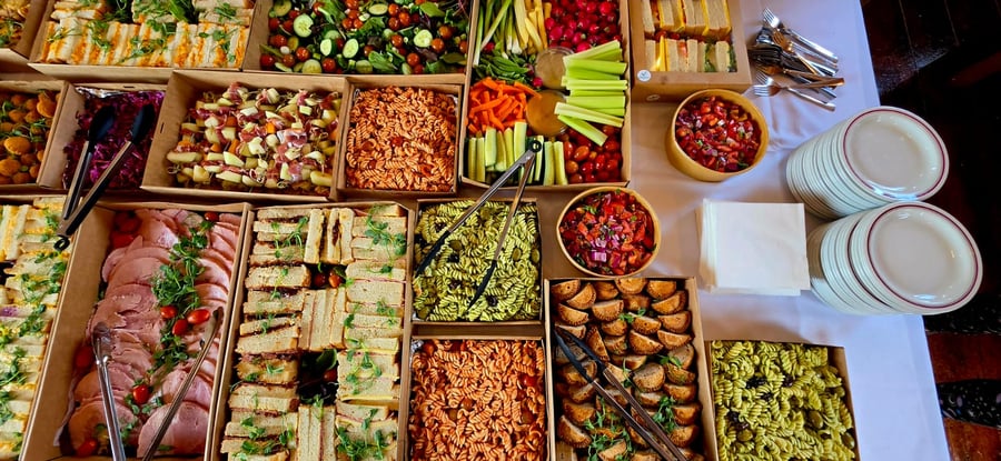 A vibrant buffet spread featuring sandwiches, pasta salads, crudités, and ham, ready for guests to enjoy