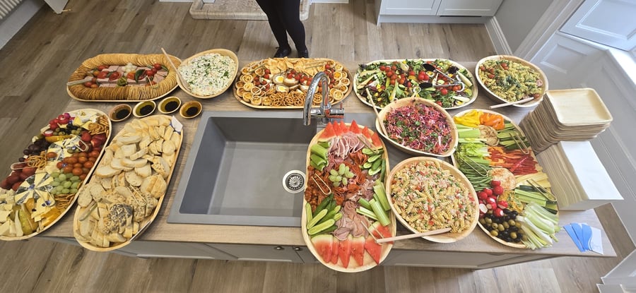 An impressive spread of buffet dishes, including charcuterie, salads, and bread, laid out on a kitchen counter