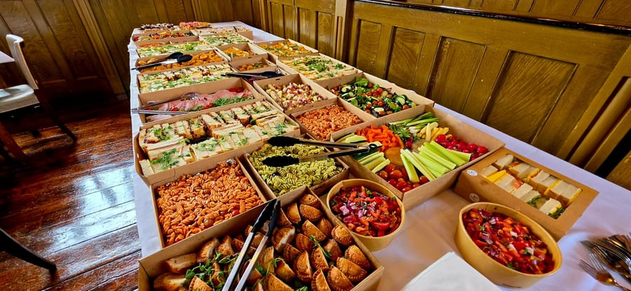 A long table laden with a variety of buffet dishes, including sandwiches, pasta salads, and fresh crudités, ready for guests
