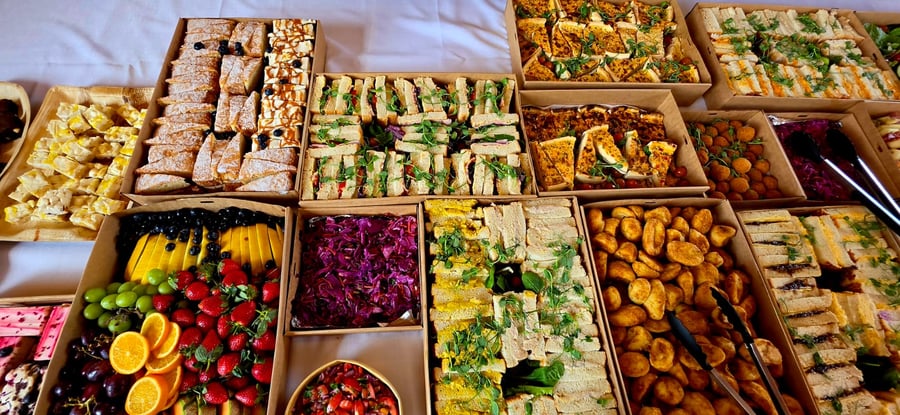An overhead view of a buffet spread featuring sandwiches, fruit, roasted potatoes, and other savoury dishes in cardboard boxes