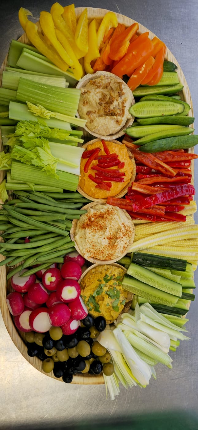 A vibrant platter of fresh crudités, including celery, peppers, radishes, and olives, served with a selection of dips