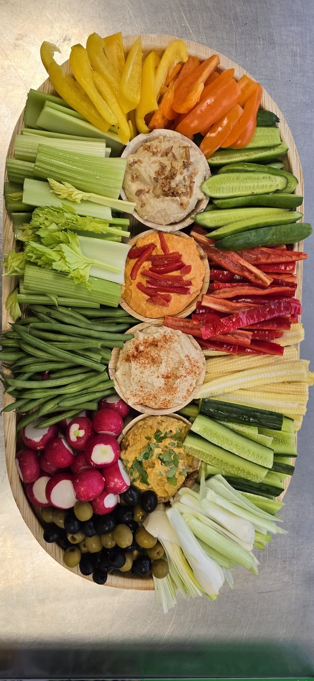 A vibrant platter of fresh crudités, including celery, peppers, radishes, and olives, served with a selection of delicious dips
