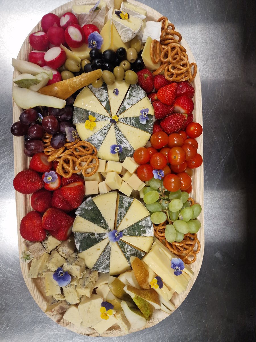 A vibrant cheese board featuring various cheeses, fresh strawberries, grapes, cherry tomatoes, radishes, olives, and pretzels