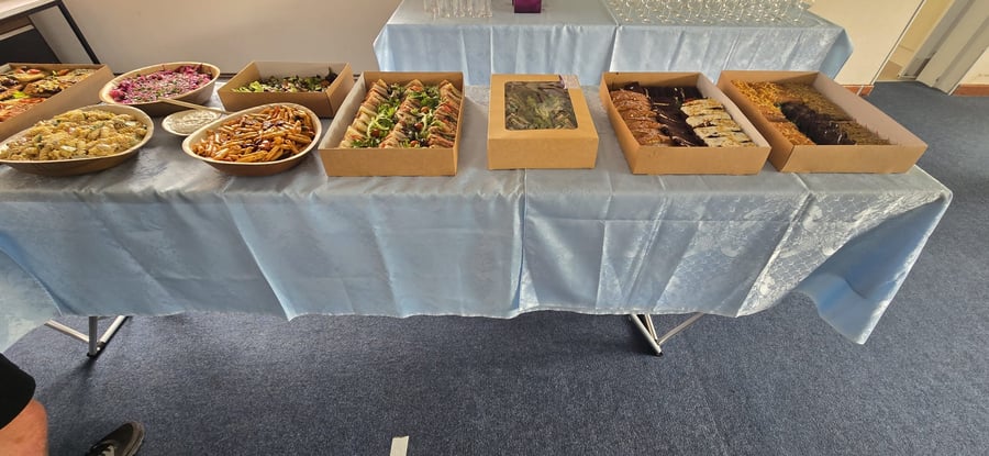 A buffet table laden with various dishes including pasta salads, sandwiches, and sweet treats, all presented in eco-friendly packaging