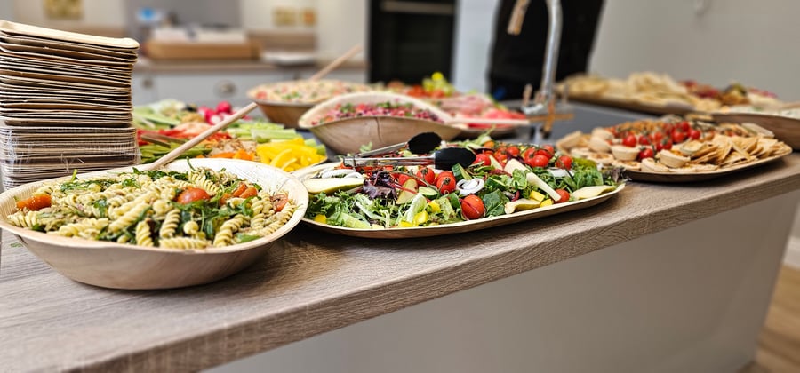 A vibrant buffet spread featuring pasta salad, mixed green salad, and various savoury tartlets, all served in eco-friendly wooden bowls