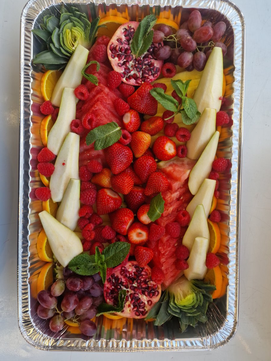 A vibrant fruit platter featuring watermelon, strawberries, raspberries, grapes, pears, oranges, and pomegranates, garnished with fresh