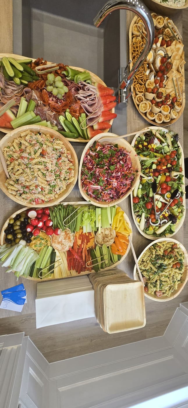 An overhead shot of a vibrant buffet spread featuring charcuterie, salads, pasta, and crudités, with eco-friendly plates ready for guests