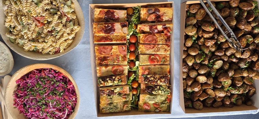 A vibrant buffet spread featuring pasta salad, red cabbage slaw, roasted potatoes, and various focaccia slices