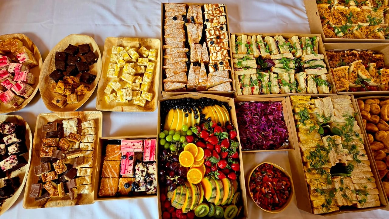 An overhead buffet in kraft boxes: sandwiches, fruit, red cabbage slaw, quiche and traybakes