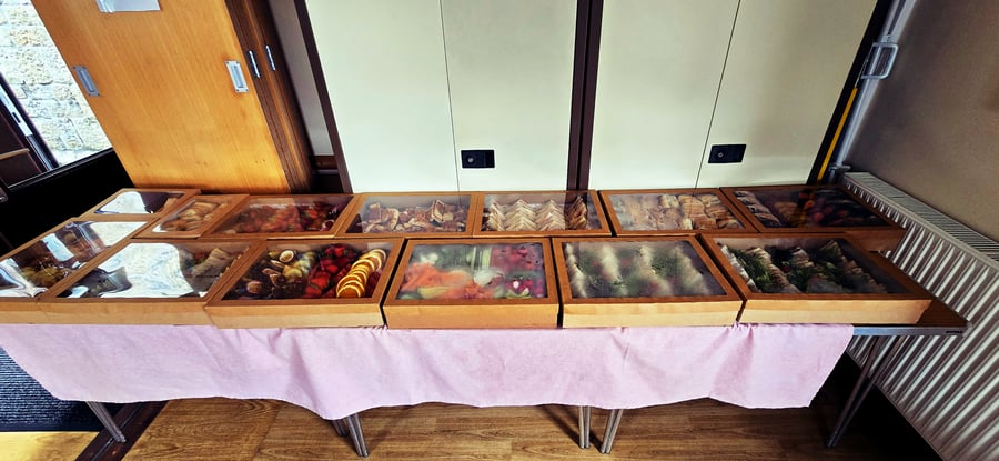 A buffet table laden with various dishes in wooden display boxes, including sandwiches, fruit, and other savoury items