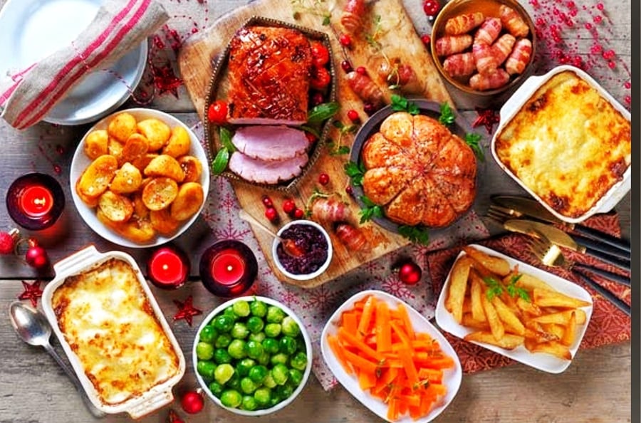 A festive Christmas buffet spread featuring roasted ham, turkey, pigs in blankets, roast potatoes, vegetables, and gratins