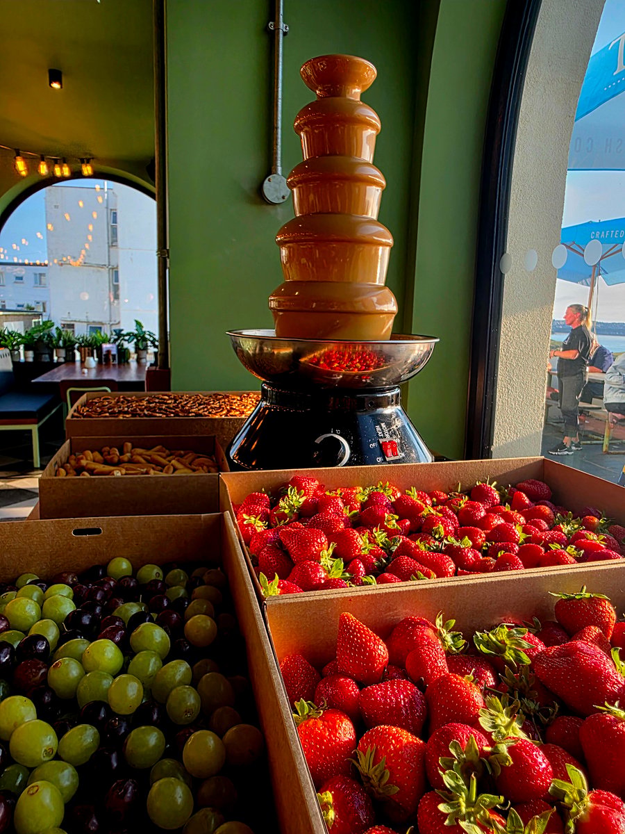 A tiered chocolate fountain with fresh strawberries, grapes, and other dipping treats, ready for guests to enjoy