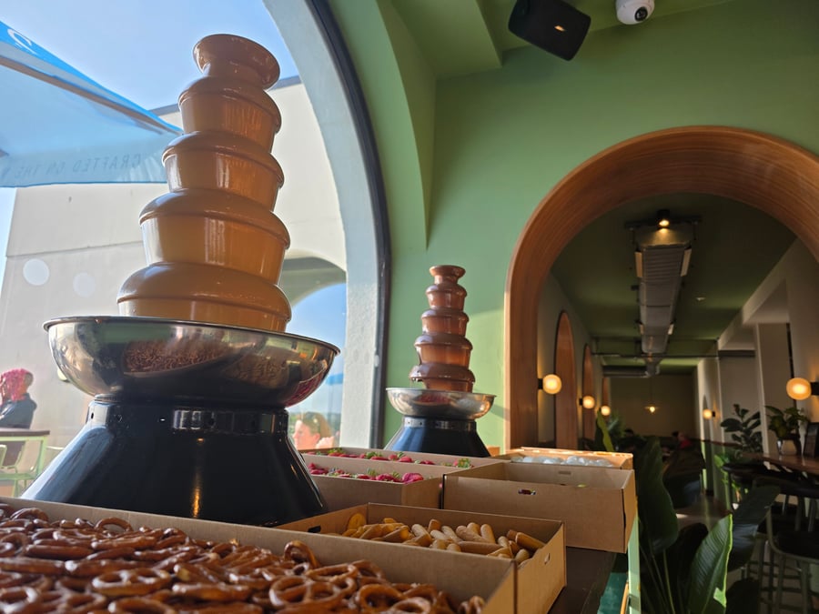 Two chocolate fountains with various dipping snacks, including pretzels, set up in a modern venue with green walls